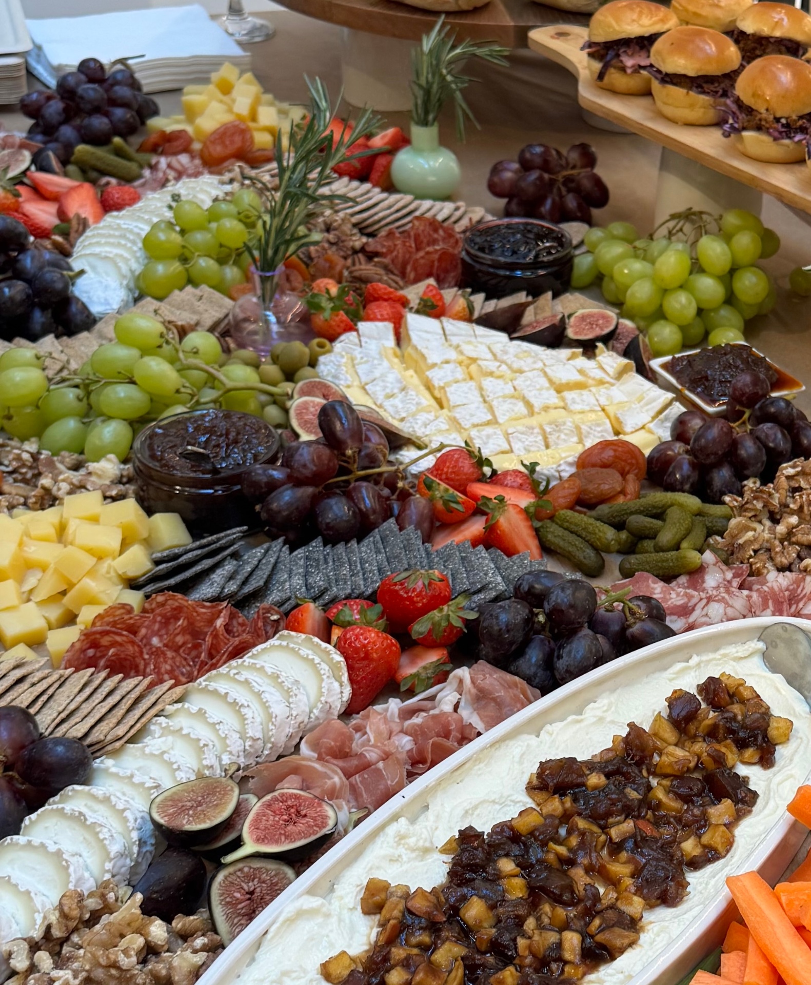 A grazing table spread with cheeses, charcuterie, fruit, and sliders